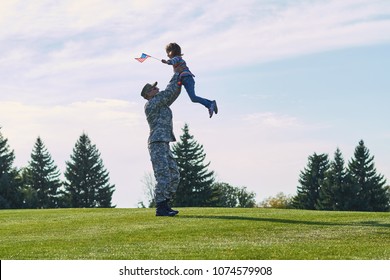 American soldier is playing with his daughter outdoor. Military father is raising up his daughter up, reunion of happy family in the summer park. - Powered by Shutterstock