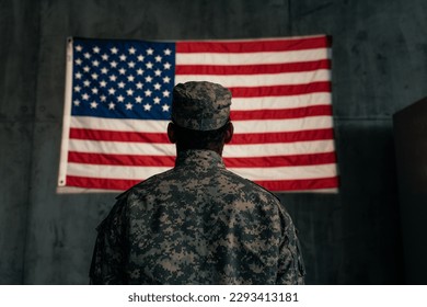 An American soldier is standing in front of an American flag on the wall, shot from the rear. - Powered by Shutterstock