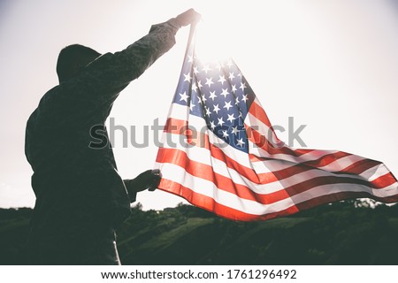 An American soldier with the US flag in his hands looks into the distance.