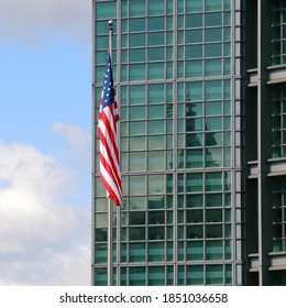 The American State Flag At The Embassy Against The Background Of The Green Glass Wall Of The Building. Square Illustration On The Theme Of USA Foreign Policy And The US Department Of State