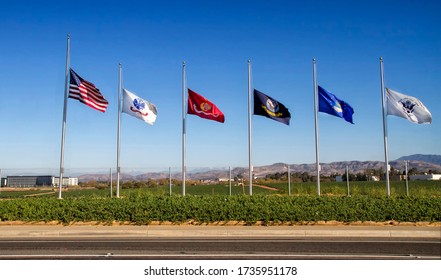 American And United States Military Flags Flying At Half Mast Against A Blue Sky In Honor Of Memorial Day.  Air Force,Army,Marines,,Navy Coast Guard Are All Represented