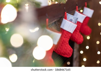 American, US dollars in сhristmas red socks for gifts on the fireplace in bokeh lights.