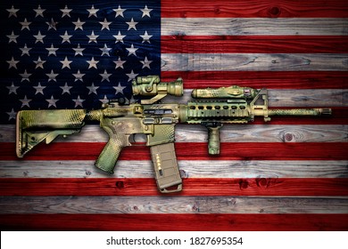 American weapon: Camo painted army carbine on wooden surface with national flag of USA
