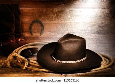 American West rodeo cowboy black felt hat on an authentic Western roping lariat lasso with leather riding boots on weathered wood floor in an old ranch barn