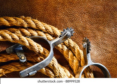 American West Rodeo Cowboy Ranching Rope With Western Riding Spurs On Old Brown Leather Grunge Background