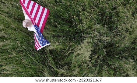 American woman covered with flag of america at sunset on wheat field