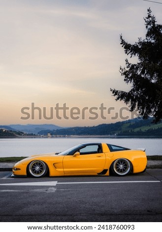 The American yellow lowered sports car after tuning against the background of a beautiful lake and mountains.