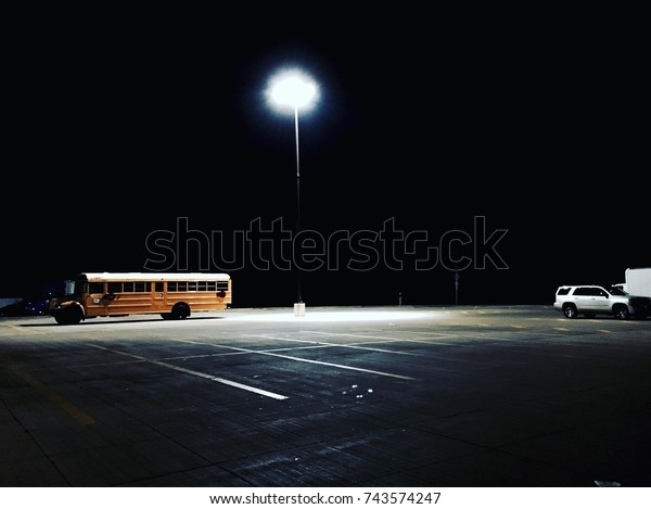 American\
yellow school bus parked in a parking lot in the night illuminated\
by a single light on the route to New\
York