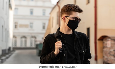 American Young Hipster Man With Hairstyle In Trendy Sunglasses In Fashionable Black Denim Jacket In Stylish Medical Black Mask Walks On Street On Sunny Day. Attractive Guy Model. Fashion 2020. Spring.