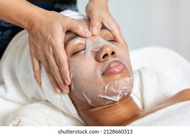 American-African Woman Uses A Mask And Has A Massage Therapist Give Her A Moisturized Facial In A Spa Salon.