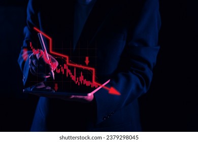 Amid a financial crisis, a focused businessman uses a tablet to analyze data, specifically a red stock graph with a significant down arrow, illustrating the alarming decrease in financial performance
