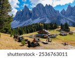 Amidst colorful autumn leaves, visitors enjoy the breathtaking Dolomites, relaxing by cozy lodges and stunning mountain views, Geisleralm Dolomites Val Di Funes in Italy Adolf Munkel Trail 