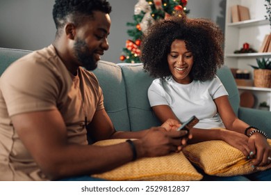 Amidst a thoughtfully decorated room, a multiracial couple enjoys each other’s company while engaging with their smartphone, capturing the essence of modern relationships in a festive backdrop. - Powered by Shutterstock