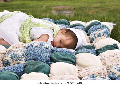 Amish Child Lying Outdoors On A Handmade Biscuit Quilt.