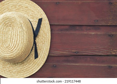 An Amish man's straw hat hangs on a red, wooden barn door