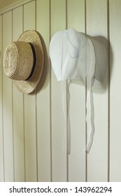 An Amish Woman's Bonnet And A Man's Straw Hat Hanging On A Wall