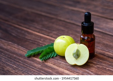 Amla fruit or indian gooseberry with green leaves and glass bottle of essential oil extract isolated on wooden table background. 