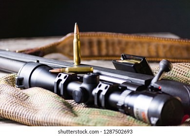 The Ammo With Black Bolt Action Rifle And Scope On The Multicam Background. Close Up.