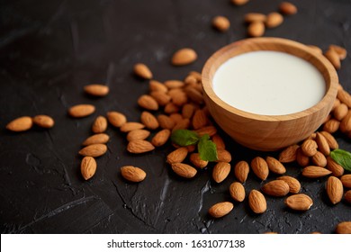 Amond seeds with bowl of fresh natural milk placed on black stone background. Side view.
