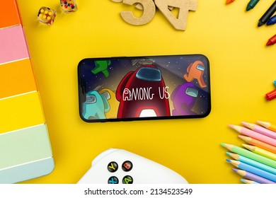 Among Us mobile game app on the smartphone screen. Yellow background with school supplies, children's accessories, video game controller. Rio de Janeiro, RJ, Brazil. February 2022.