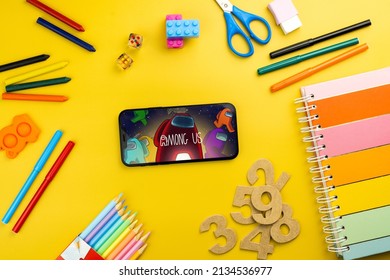 Among Us mobile game app on the smartphone screen. Yellow background with school supplies, children's accessories, video game controller. Rio de Janeiro, RJ, Brazil. February 2022.