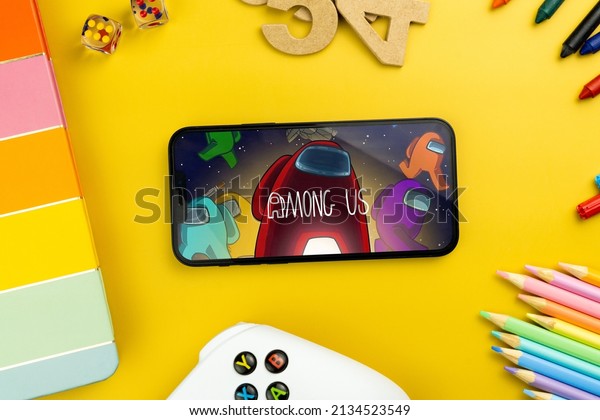 Among Us mobile\
game app on the smartphone screen. Yellow background with school\
supplies, children\'s accessories, video game controller. Rio de\
Janeiro, RJ, Brazil. February\
2022.