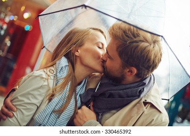 Amorous young couple kissing under umbrella - Shutterstock ID 330465392