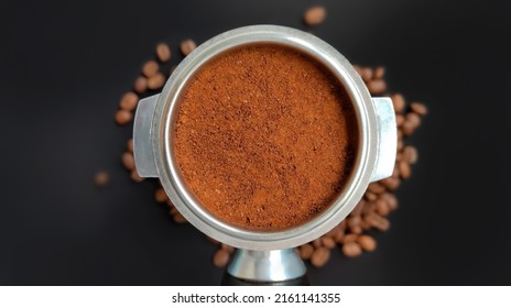 Amped Puck Of Coffee Grounds Within Basket Of Portafilter And Coffee Beans Spilled Around In A Dark And Moody Scene Of Natural Light.