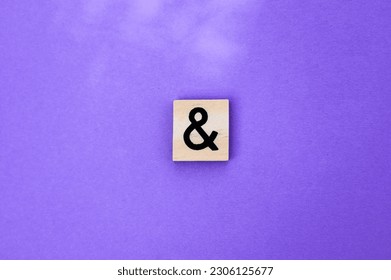 Ampersand symbol on a wooden cube on a purple background with copy space.