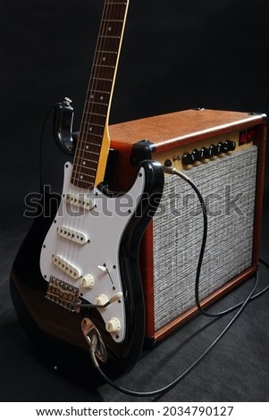 Amplifier for electric guitar with black guitar on the black background. 