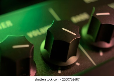 Amplifier knobs, selective focus, shallow depth of field. Guitar amp audio amplifier control panel knobs seen under green and purple stage lights. Black control panel and knobs, white markers