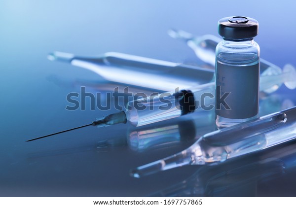 ampoule, glass vials and a medical\
syringe with a coronavirus vaccine on a blue\
background