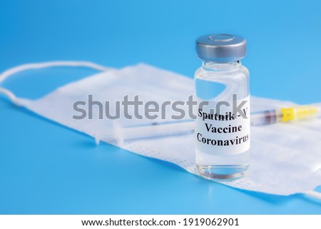 ampoule with vaccine Sputnik-V and medical mask with syringe on blue background, vaccination, treatment from coronavirus, covid-19, SARS-CoV-2, closeup