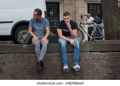 Amsterdam - CIRCA August 2018: 2 men sitting together on a canal bank. Street background. - Shutterstock ID 1482980669
