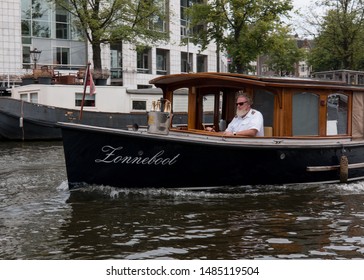 Amsterdam - CIRCA August 2018: Mature Man With A White Beard Driving A Motor Boat Down A Street Canal.