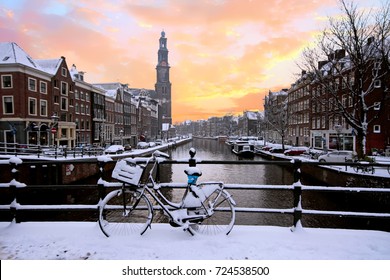 Amsterdam covered with snow with the Westerkerk in winter in the Netherlands at sunset