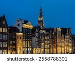 Amsterdam damrak and the tower of the oude kerk in the evening, picturesque dutch houses by the canal