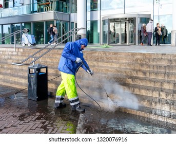 Amsterdam, February 2019. Worker in waterproof clothing cleaning the steps in front of a building with a high pressure cleaner
