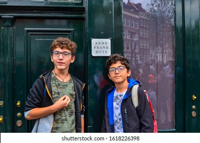 Amsterdam, Holland, August 2019. Anne Frank's House Is A Destination For Many Tourists: The Crowd In The Street Is Remarkable. Two Young People Stand In Front Of The Plaque For A Souvenir Photo.