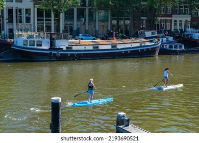 Amsterdam, The Netherlands - 22 June 2022: Two People On Paddle Boards On Amsterdam Canal