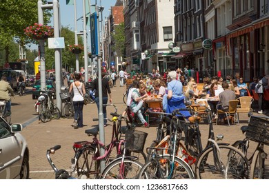 Amsterdam, Netherlands - 7/15/2013: A Busy Sidewalk With People Walking And A Sidewalk Cafe In Amsterdam, Netherlands