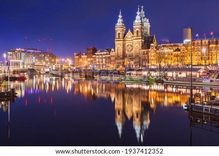 Amsterdam, Netherlands city center view with riverboats and the  Basilica of Saint Nicholas at night.