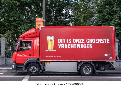 Amsterdam, the Netherlands - July 1, 2019: Red Amstel beer delivery truck although it claims to be the greenest truck. Driver active. Image of full Amstel bier glass. Green foliage.
