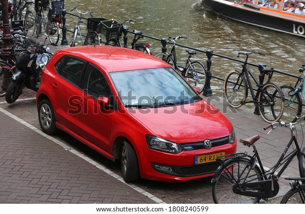 AMSTERDAM,\
NETHERLANDS - JULY 10, 2017: Red Volkswagen Polo Cross small city\
car parked by the canal in Amsterdam. Netherlands has 528\
registered cars per 1,000\
inhabitants.