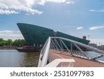 Amsterdam, Netherlands - June 30, 2019: View of NEMO Science Museum with a pedestrian bridge in the foreground.