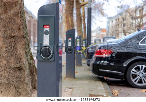 AMSTERDAM,\
THE NETHERLANDS - November 19, 2018: Power supply connect to\
electric vehicle for charging battery, Charging an electric car in\
public station by the street, Green\
energy.