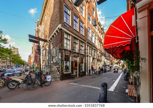 Amsterdam, Netherlands -\
October 1 2016: Bicycles and cars park alongside a corner cafe\
covered with colorful graffiti in the tourist section of Amsterdam\
in early autumn