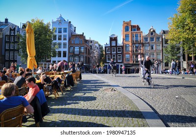 Amsterdam, The Netherlands - October 16, 2016: Young people sit at a sidewalk cafe in the sun on a canal with autumn trees in Amsterdam, The Netherlands on October 16, 2016
