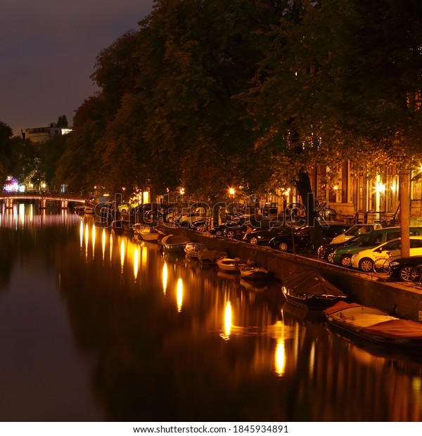Amsterdam street night illumination.\
Reflections of street lamps light on the water. Boats moored along\
the canal.\
Netherlands