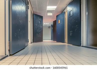 AMSTERDAM/NETHERLANDS-FEBRUARY 24 2019: An empty corridor of a prison with tiles on the floor and open steel cell doors on which texts are scratched The cells are empty